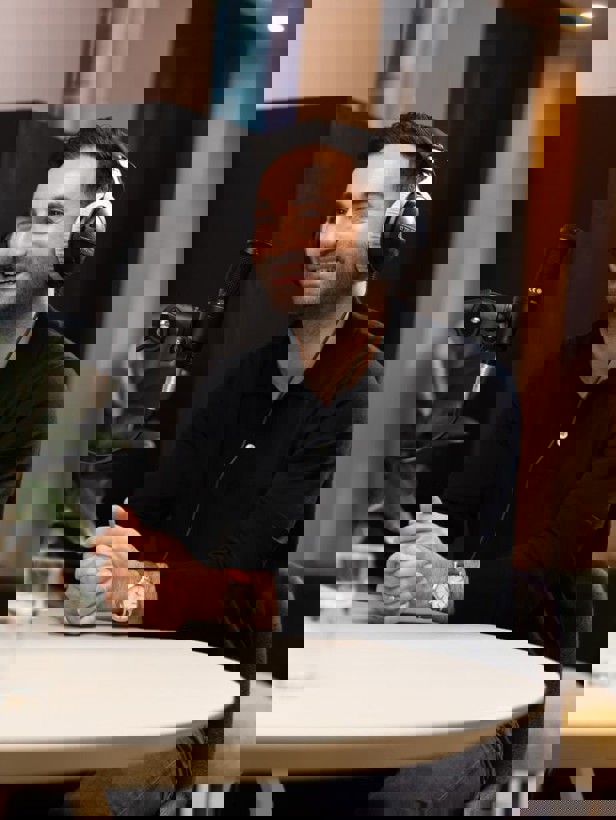 Onur in zwart T-shirt en met hoofdtelefoon, zittend bij een microfoon in een moderne setting.