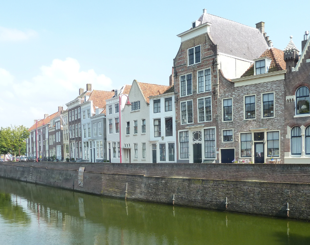 Historische gebouwen aan een kanaal in een stad, zichtbaar onder een heldere blauwe lucht.