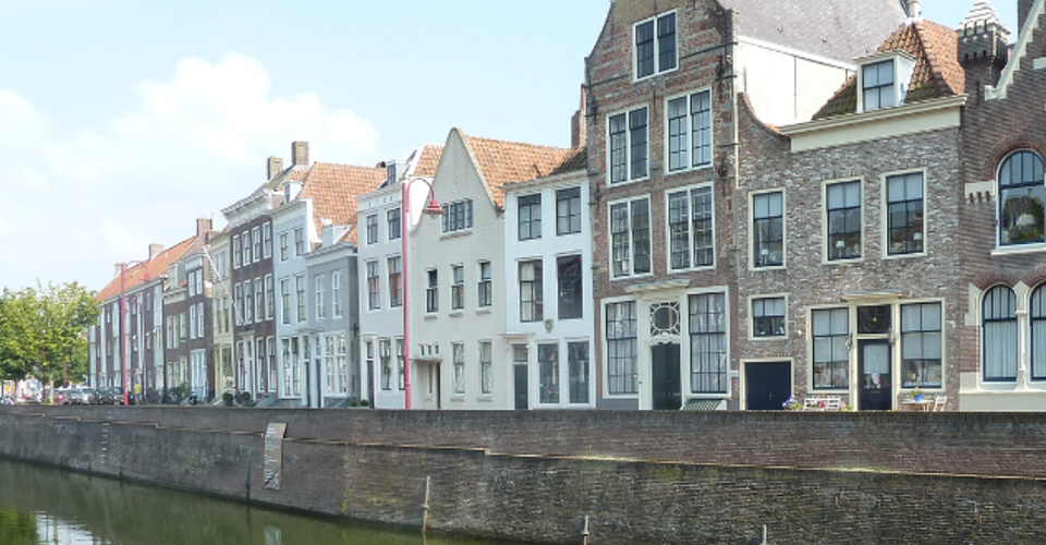 Historische gebouwen aan een kanaal in een stad, zichtbaar onder een heldere blauwe lucht.