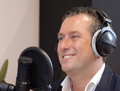 Wouterlangeveld met een microfoon en koptelefoon in een studio, die zich voorbereidt op een opname.