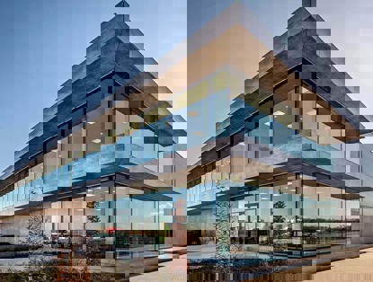 Modern office building with a glass façade and concrete elements, situated in a green environment.