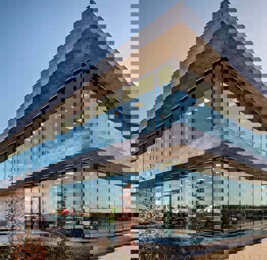 Modern kantoorgebouw met een glazen façade en betonnen elementen, omgeven door groen.