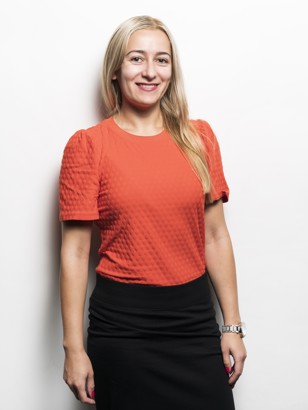 Helena Krivorucsko in een oranje top met pofmouwen en een zwarte rok, poserend voor een witte achtergrond.