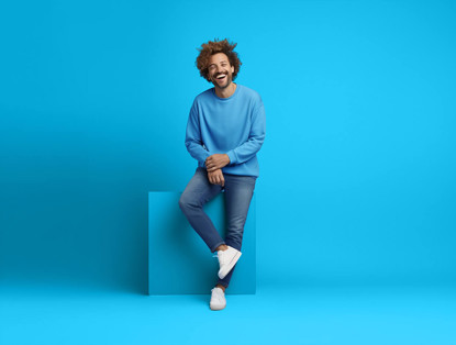 Jongeman in een blauwe trui en jeans leunt relaxed tegen een blauwe achtergrond.