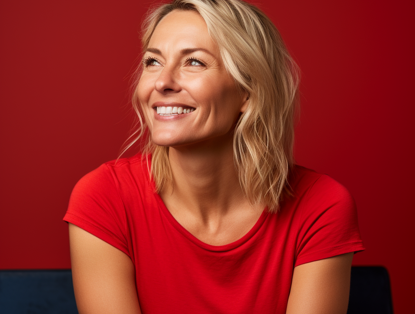 Vrouw in een rood shirt, zittend tegen een helderrode achtergrond, met schouderlang haar en een ontspannen houding.