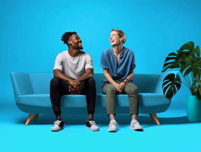 Twee mensen zitten op een lichtblauwe bank voor een felblauwe achtergrond, omringd door een groene plant.